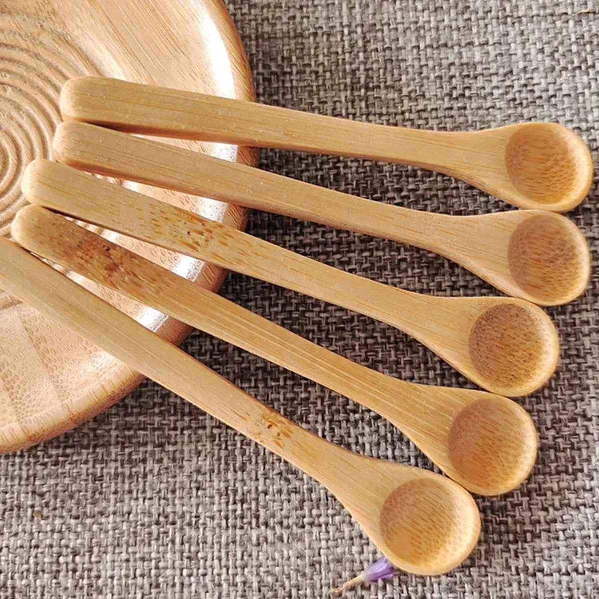 Cinq petites cuillères en bambou naturel de 9cm présentées en éventail sur un support tressé, idéales pour le dosage du café et des épices.