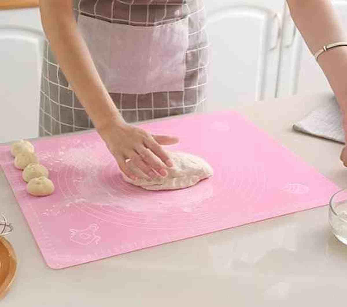 Gros plan d'une personne pétrissant de la pâte sur le tapis en silicone rose PâtissiPro, montrant la surface graduée et l'aspect relaxant de la pâtisserie.