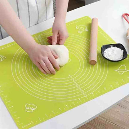Tapis de pétrissage en silicone vert avec graduations et repères de mesure, accompagné d'un rouleau à pâtisserie en bois et de farine sur un plan de travail.