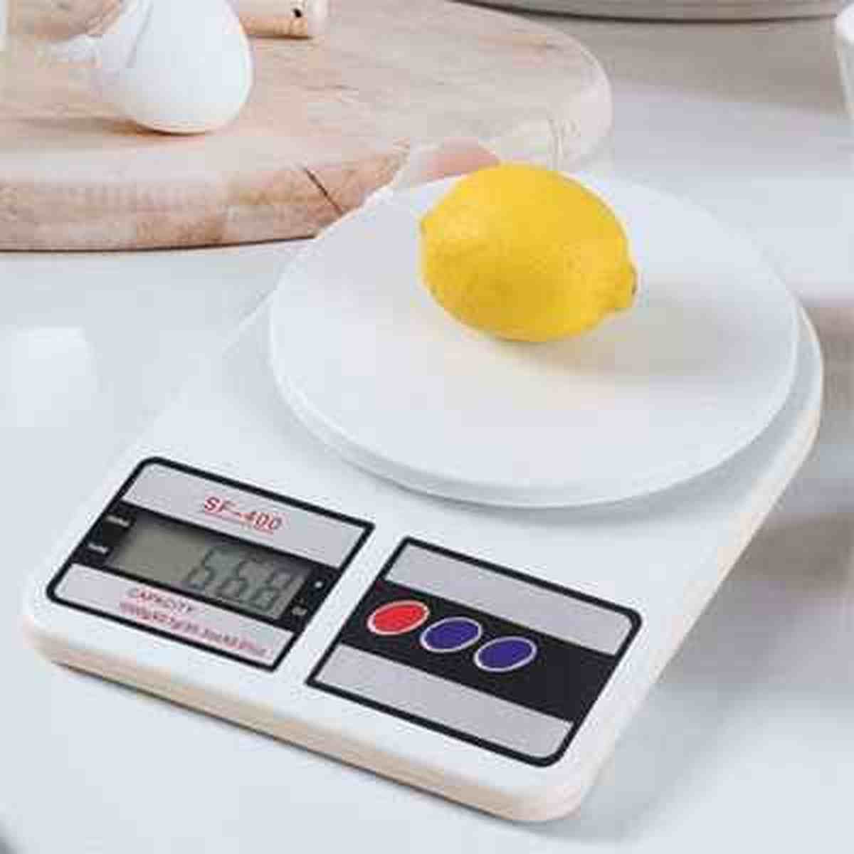 Balance de cuisine blanche Precision Pro pesant un citron jaune (66g) à côté d'un œuf blanc sur une planche en bois.