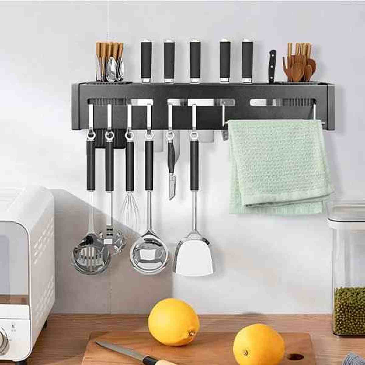 Barre magnétique murale en acier noir organisant des couteaux de cuisine, des ustensiles suspendus et un torchon au-dessus d'un plan de travail.