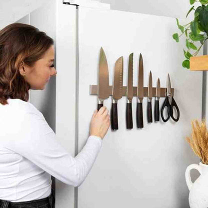 Femme utilisant un porte-couteaux magnétique en inox fixé au mur d'une cuisine lumineuse, entouré d'accessoires de décoration.