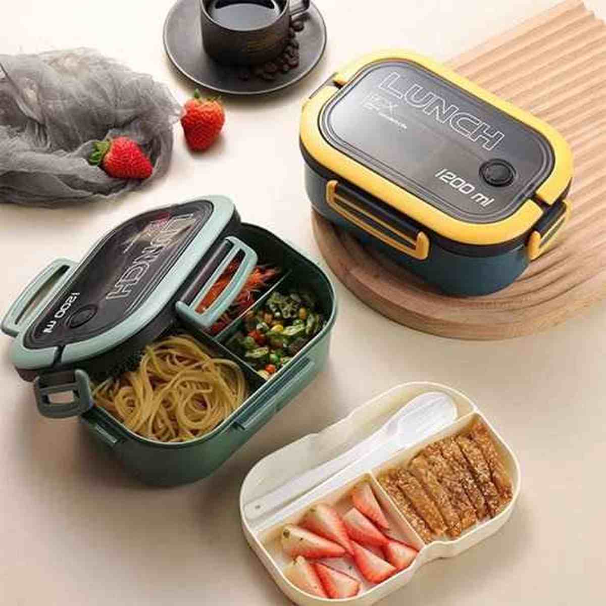 Vue de dessus d'une lunch box écologique verte ouverte montrant des compartiments remplis de pâtes, légumes et fraises, avec une boîte à couverts assortie
