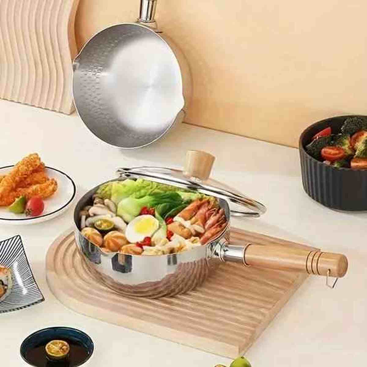 Casserole en acier inoxydable avec manche en bois remplie d'une soupe de légumes et crevettes, posée sur une planche en bois.