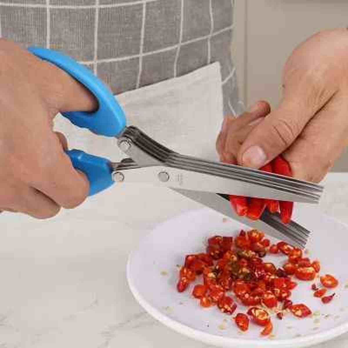 Gros plan des ciseaux de cuisine MultiLayersScissor découpant des piments rouges frais en fines lamelles sur une assiette