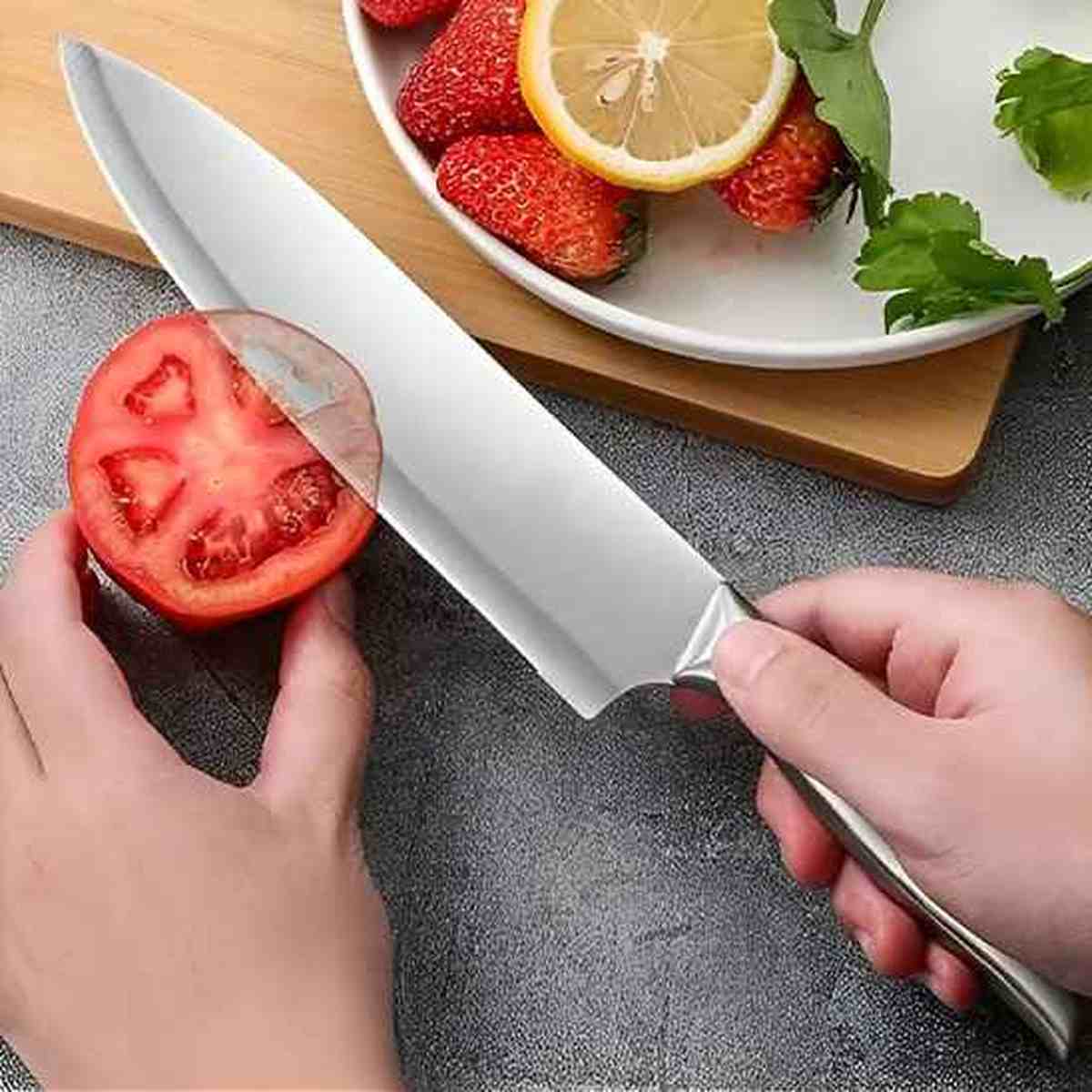 Gros plan d'une main tenant un couteau de chef professionnel en inox tranchant une tomate avec facilité sur une planche de cuisine