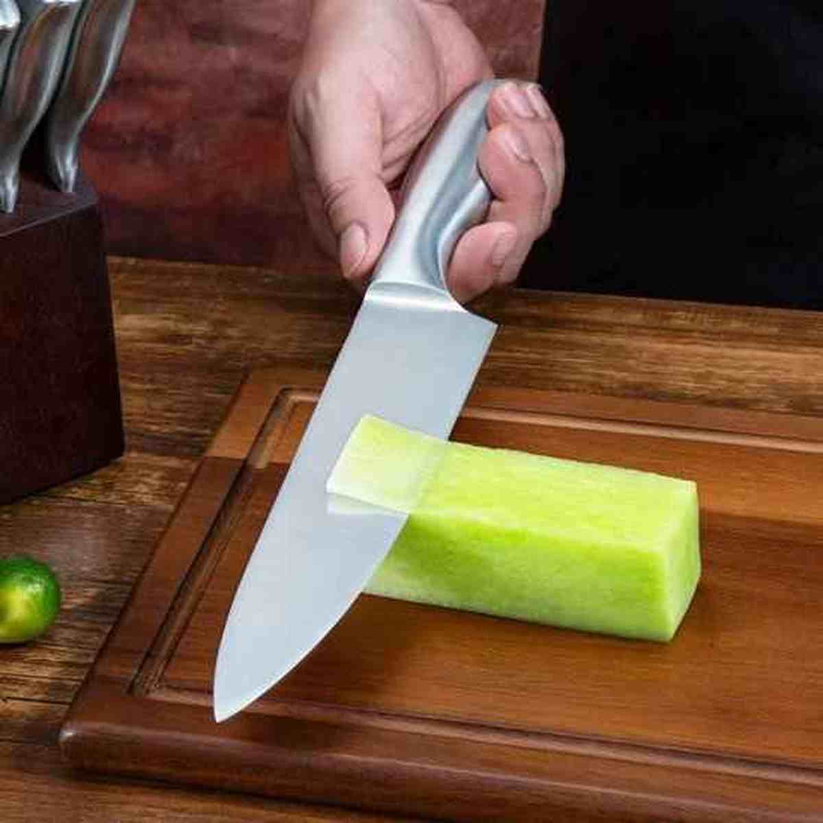 Couteau de chef professionnel en acier inoxydable découpant un légume sur une planche à découper en bois massif.