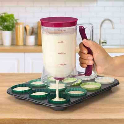 Entonnoir à piston transparent gradué avec couvercle bordeaux, utilisé pour verser de la pâte précisément dans des moules à muffins verts.