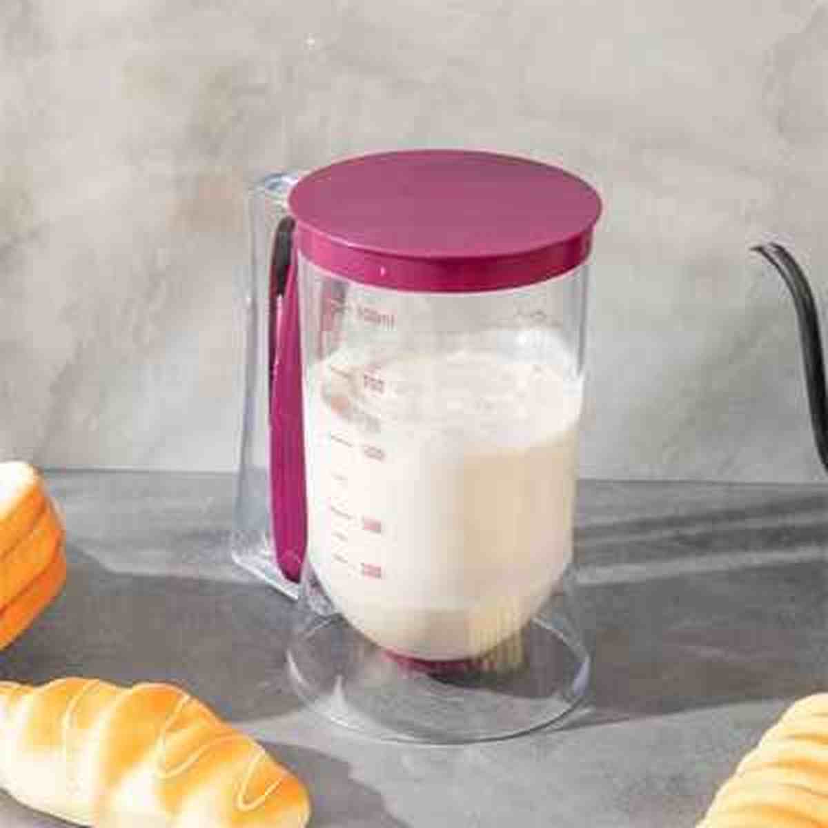 Entonnoir à piston transparent gradué avec socle de rangement, rempli de pâte à gâteau pour une cuisine propre et précise.