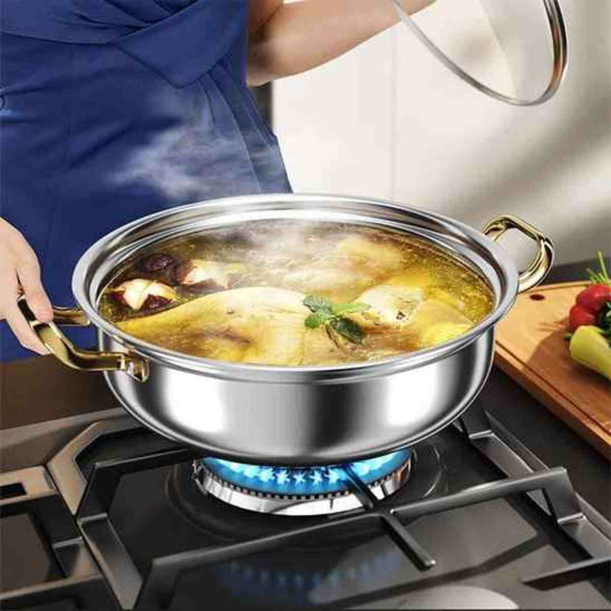 Gros plan d'un faitout en fonte émaillée sur un brûleur à gaz, contenant un bouillon de poulet aux herbes en ébullition avec de la vapeur