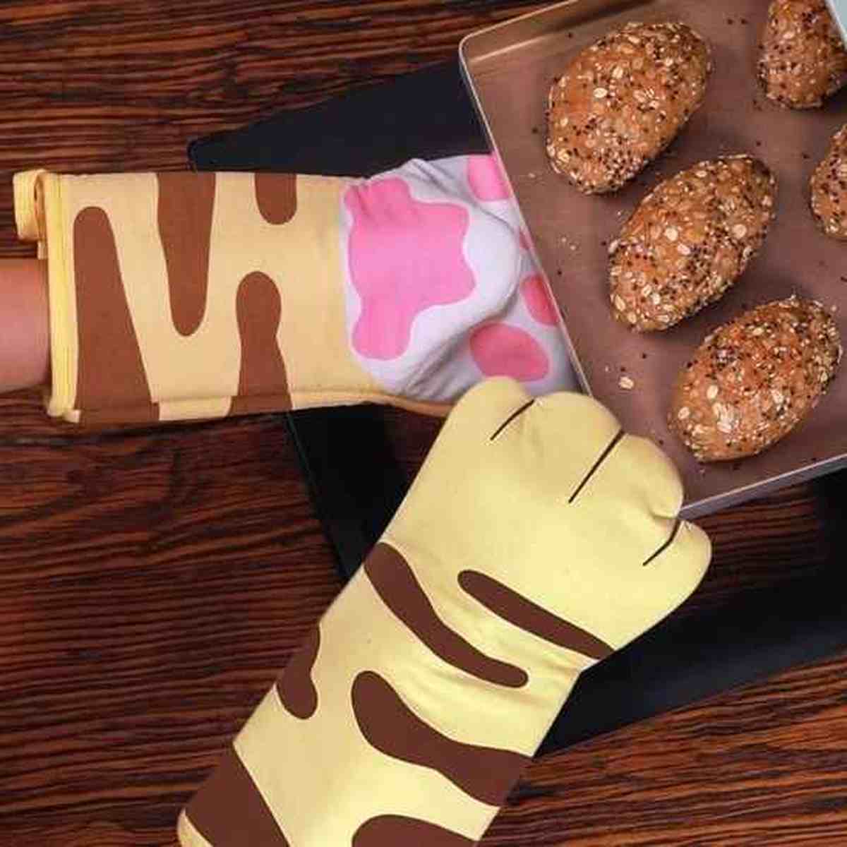 Paire de gants de cuisine résistants à 300°C avec motifs cœurs roses, utilisés pour sortir un plat de muffins chauds du four en toute sécurité.