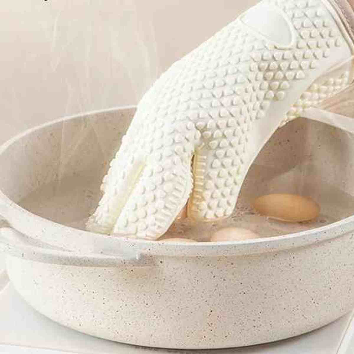 Gant de cuisine ThermoProtect en silicone blanc utilisé pour retirer des aliments d'une eau bouillante, démontrant son étanchéité et sa résistance thermique.