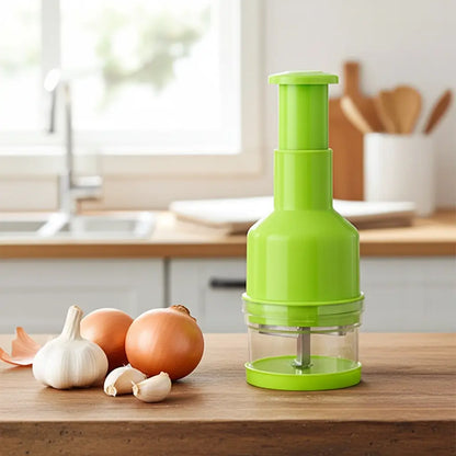 Hachoir manuel à pression vert pour oignons et ail posé sur un plan de travail en bois dans une cuisine lumineuse