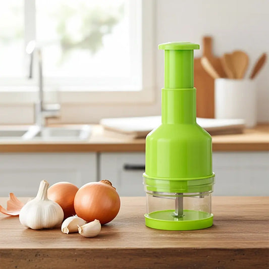 Hachoir manuel à pression vert pour oignons et ail posé sur un plan de travail en bois dans une cuisine lumineuse