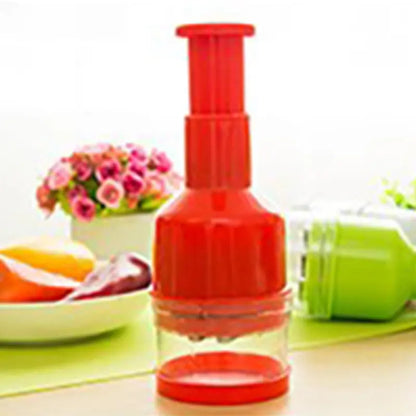 Hachoir manuel à pression rouge pour oignons et ail avec accessoires sur un plan de travail de cuisine.
