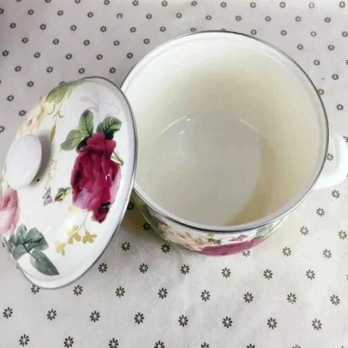 Vue de dessus de l'intérieur blanc d'une casserole en céramique émaillée avec son couvercle fleuri posé à côté sur une nappe à motifs
