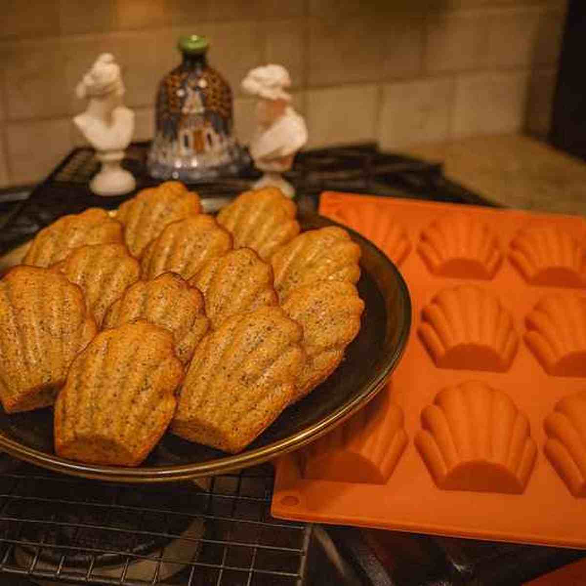 Assiette de madeleines dorées à côté du moule en silicone orange PâtissiPro, illustrant une cuisson homogène et un démoulage sans effort.