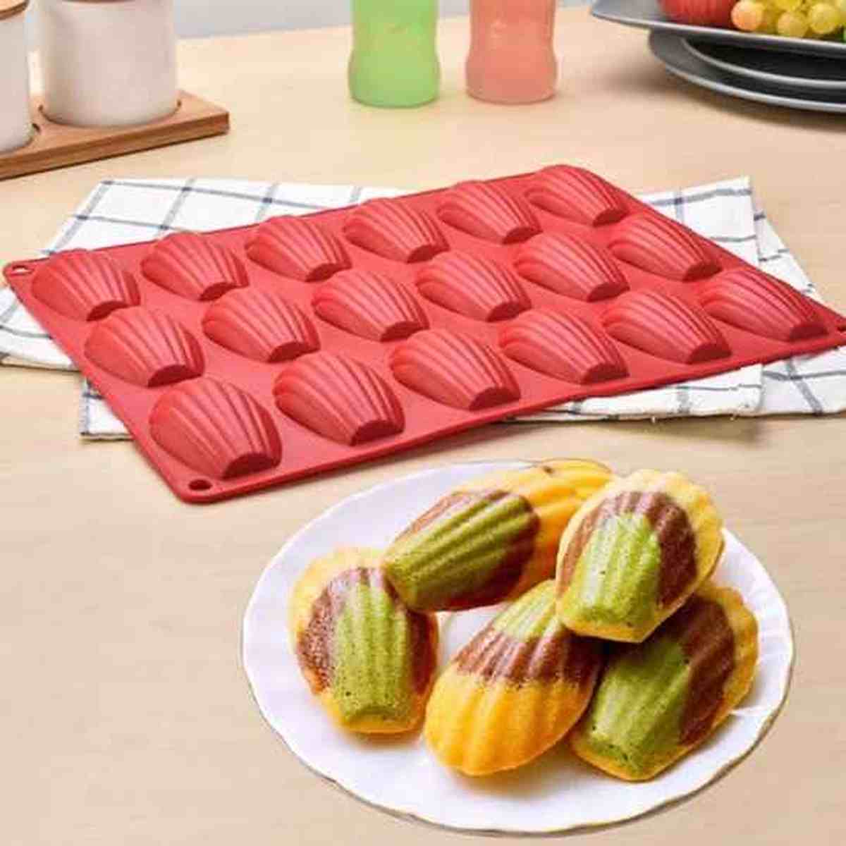 Madeleines bicolores chocolat et pistache avec une belle bosse, cuites dans le moule à madeleines en silicone rouge PâtissiPro à 12 empreintes.