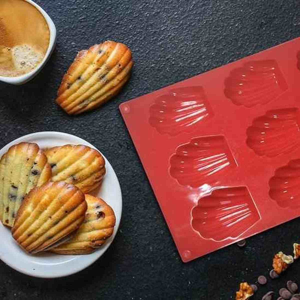 Moule à madeleines en silicone rouge PâtissiPro avec 12 empreintes, à côté de madeleines aux pépites de chocolat pour illustrer la précision du démoulage.