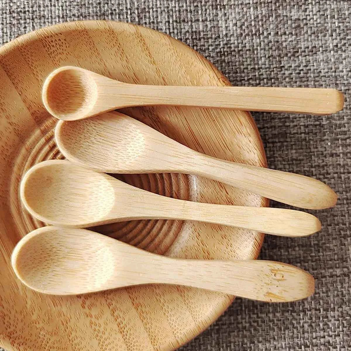 Quatre petites cuillères en bambou naturel de 9cm disposées dans un bol en bois, idéales pour le miel ou les condiments