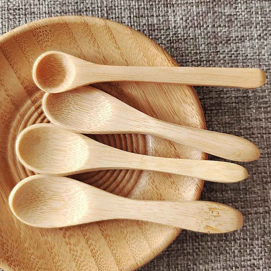 Quatre petites cuillères en bambou naturel de 9cm disposées dans un bol en bois, idéales pour le miel ou les condiments