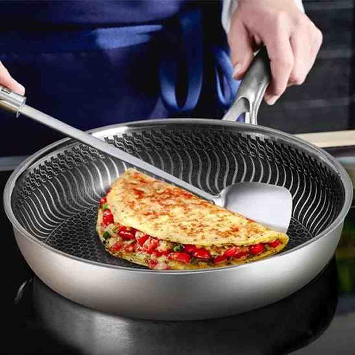 Cuisson d'une omelette dans la poêle en inox à revêtement alvéolé, montrant les propriétés anti-adhésives et la facilité d'utilisation.