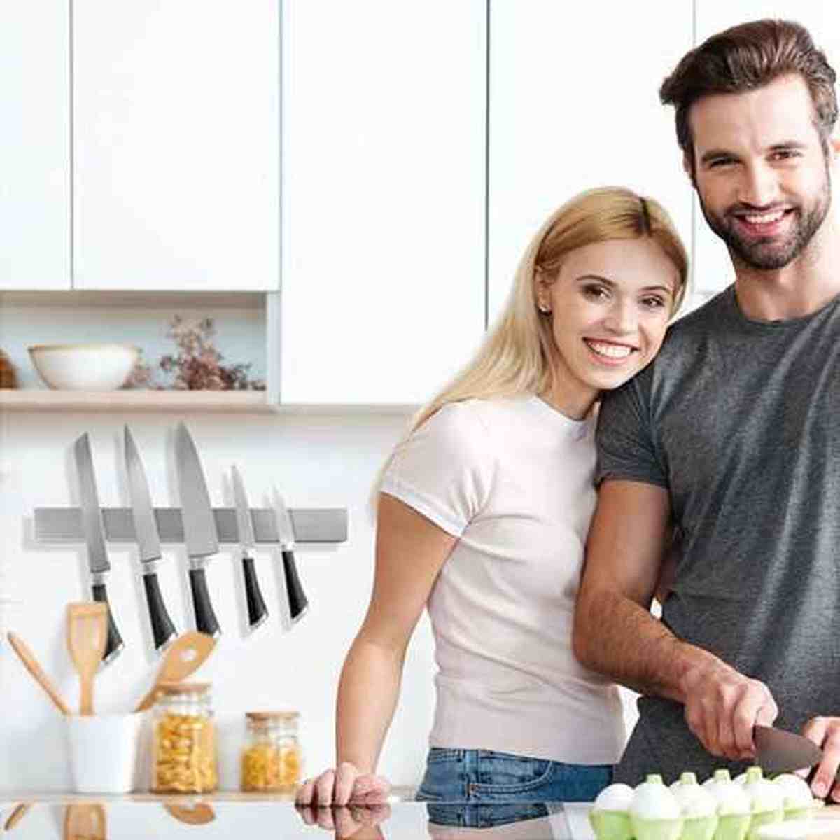 Couple souriant cuisinant ensemble dans une cuisine moderne avec une barre magnétique porte-couteaux en inox fixée au mur.