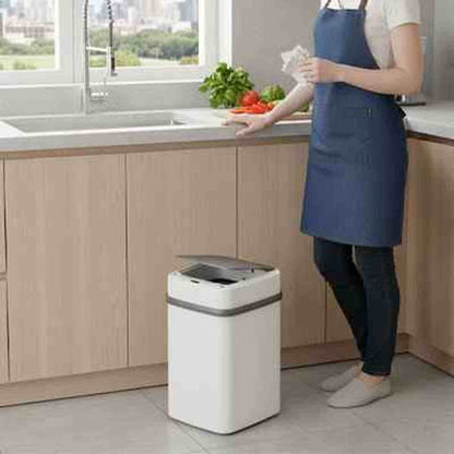 Femme en tablier bleu debout dans une cuisine à côté de la poubelle automatique Design Fresh, illustrant sa hauteur ergonomique.