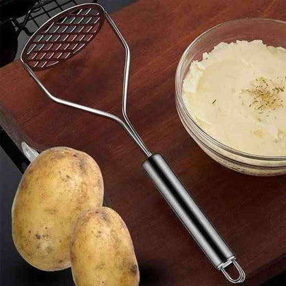 Presse-purée en acier inoxydable posé sur un plan de travail avec un bol de purée lisse et des pommes de terre entières.
