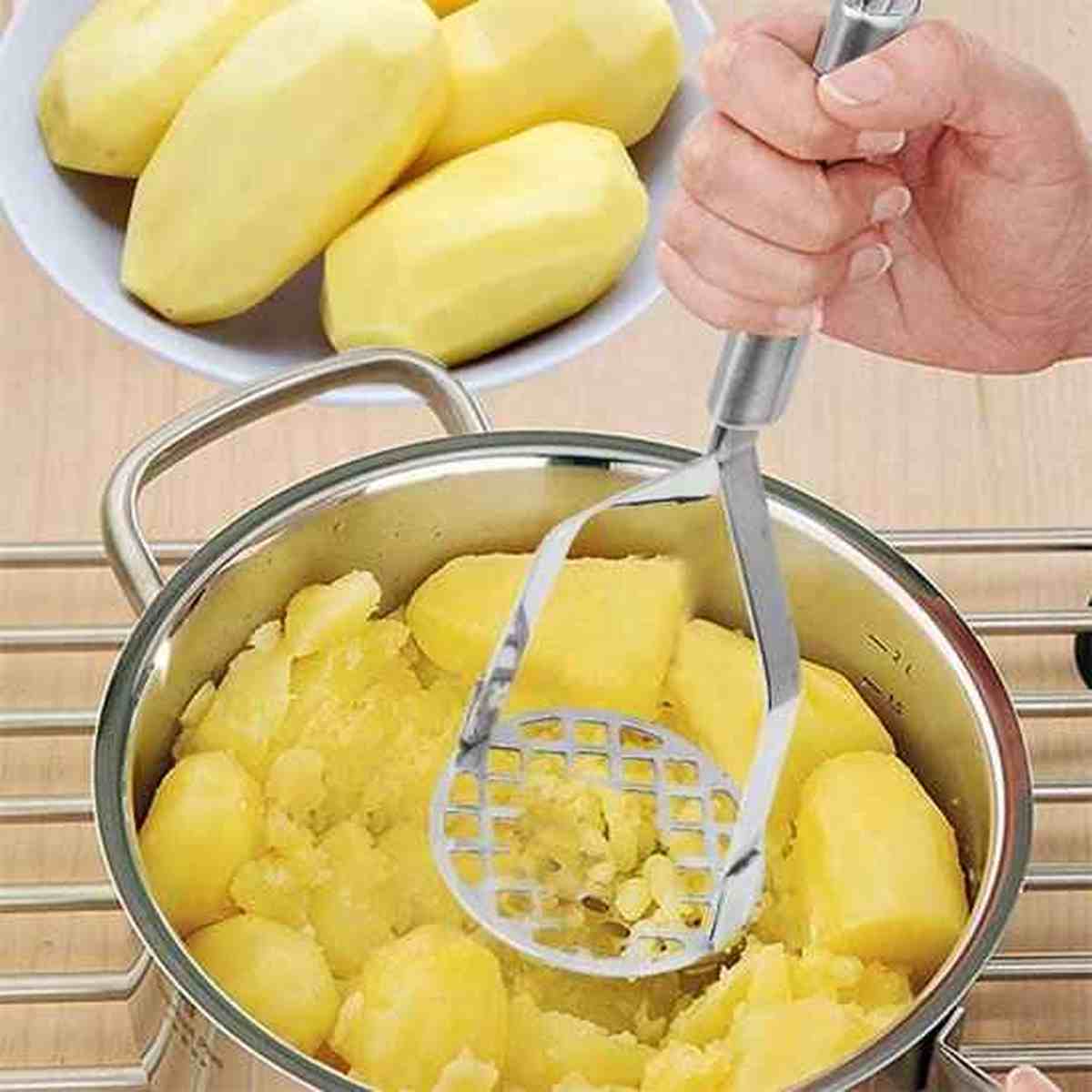 Presse-purée manuel en acier inoxydable écrasant des pommes de terre directement dans une casserole en inox