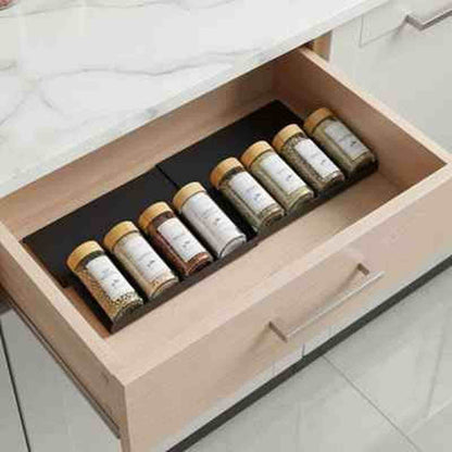 Organisateur de tiroir pour épices noir extensible ajusté sur mesure dans un tiroir de cuisine en bois clair.