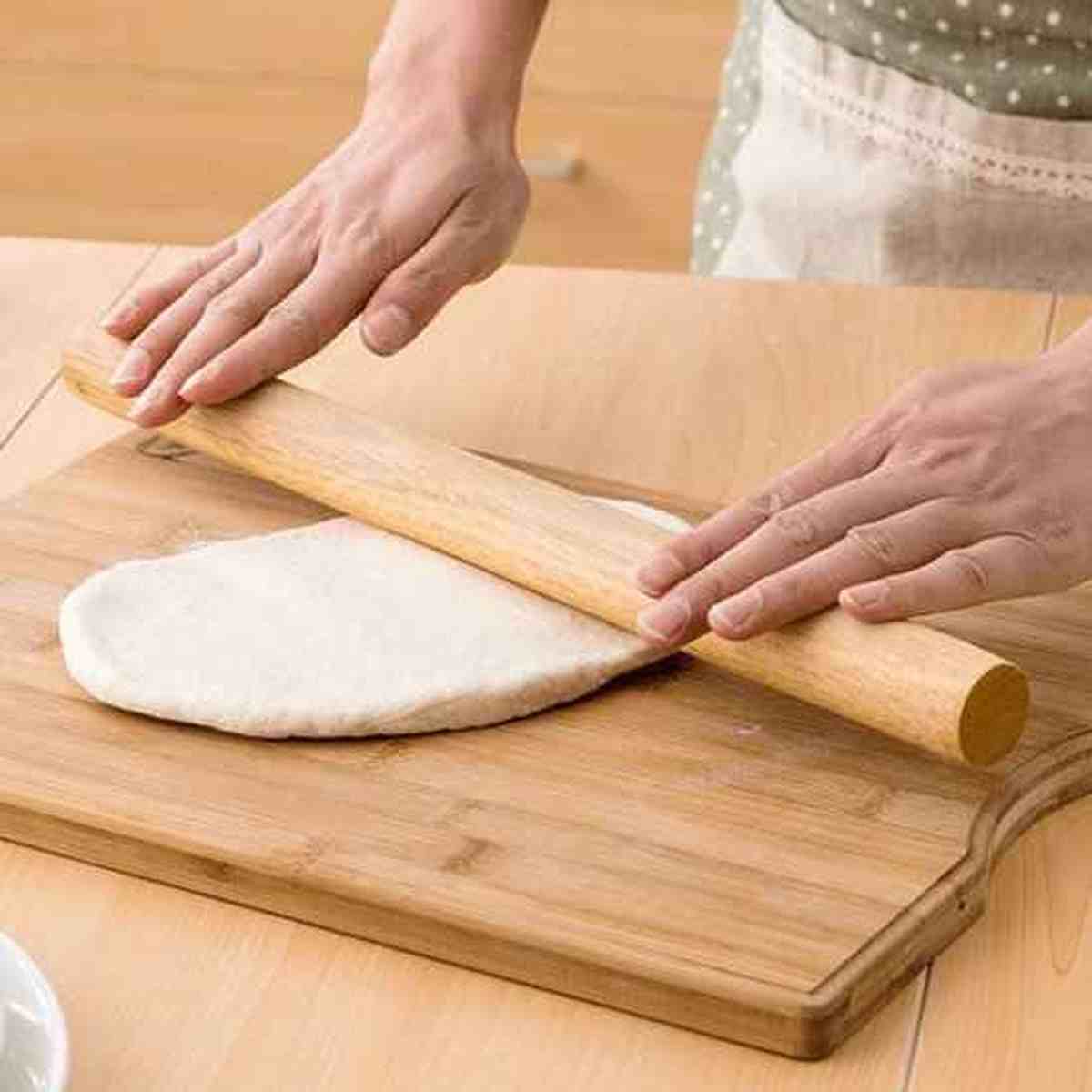 Utilisation du rouleau à pâtisserie en bois massif Artisan Pro pour étaler une pâte à pizza uniforme sur une planche en bois.