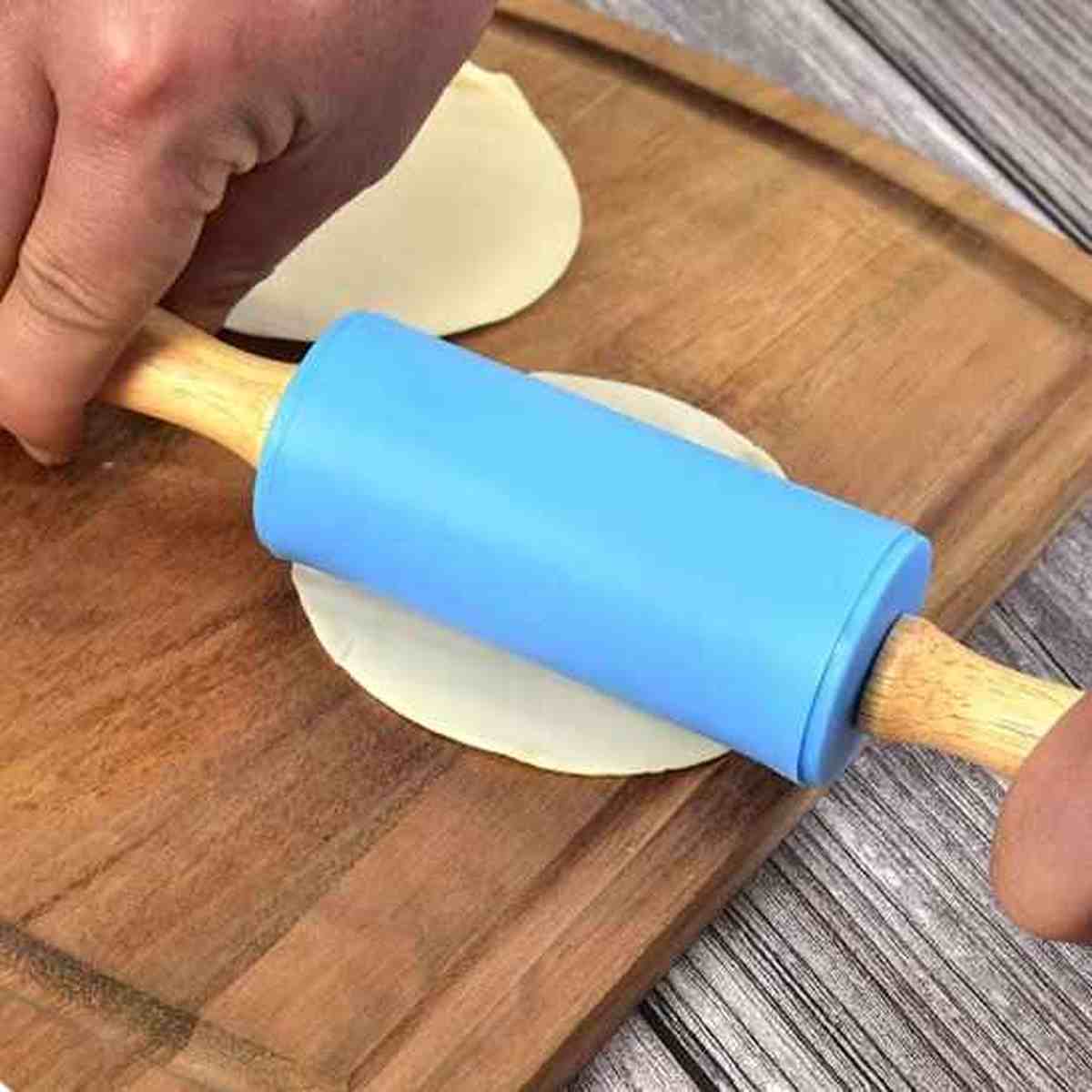 Main utilisant le rouleau à pâtisserie en silicone bleu Artisan Pro pour étaler avec précision de petites pâtes rondes sur une planche en bois.