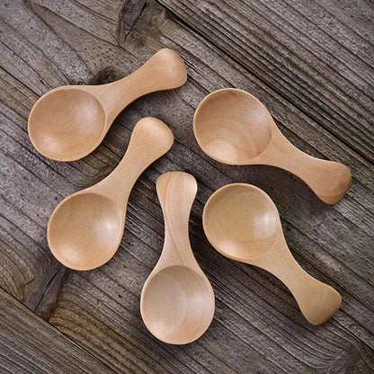 Alignement de cinq mini cuillères de dosage en bois naturel posées sur une surface en bois brut, montrant la finition lisse et artisanale