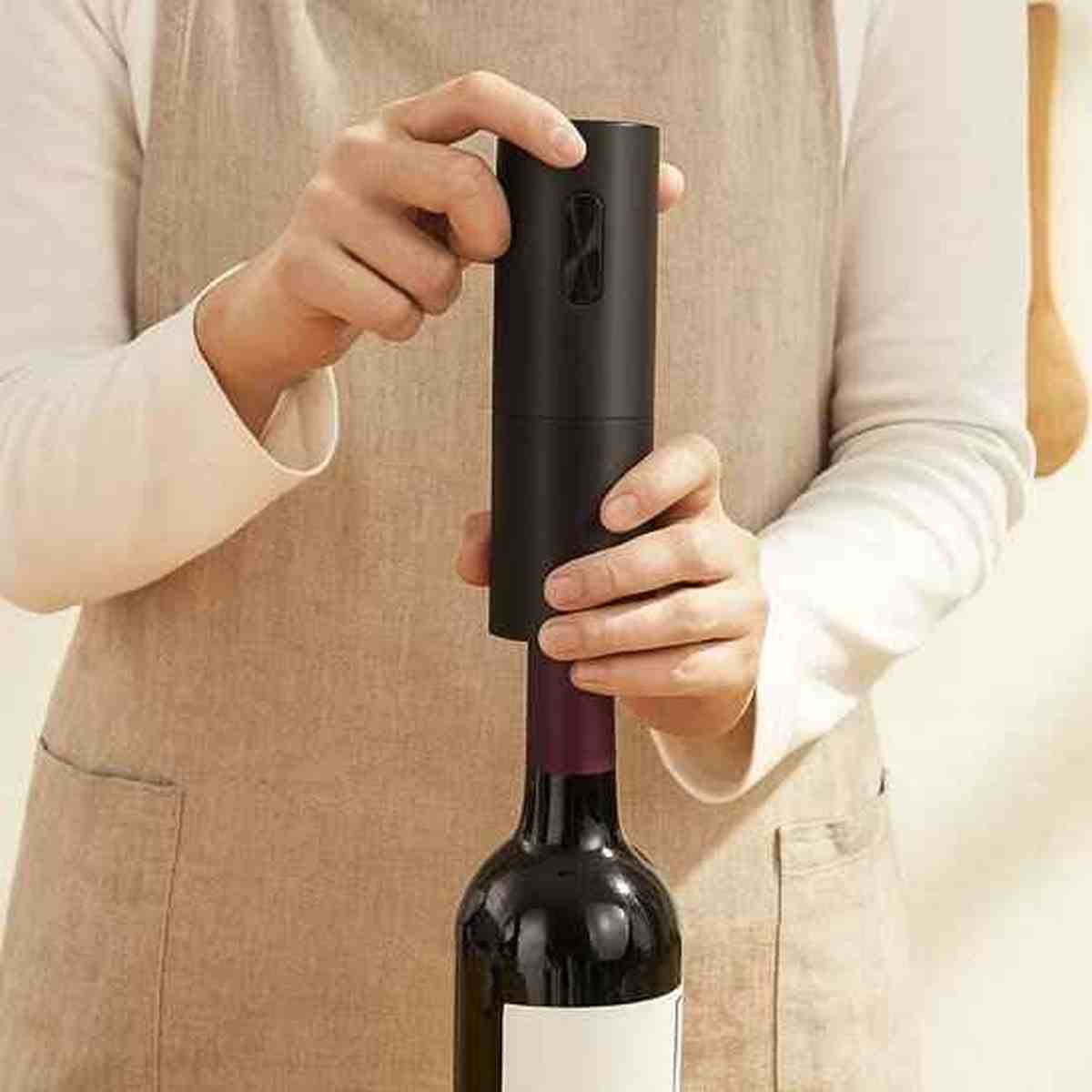 Gros plan sur le tire-bouchon électrique noir extrayant un bouchon de liège d'une bouteille de vin rouge avec facilité.