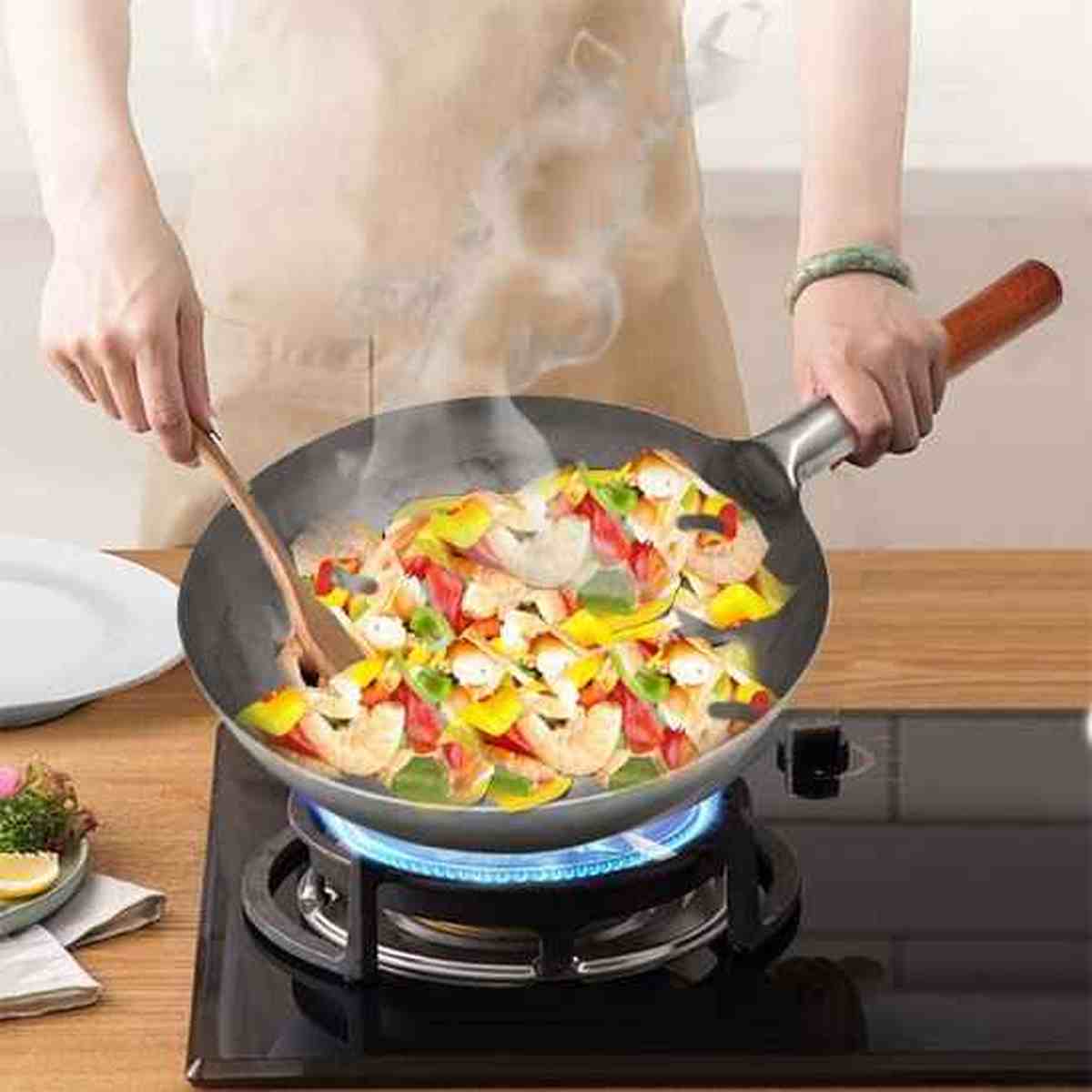 Wok professionnel en acier au carbone utilisé pour cuisiner des crevettes et des légumes frais sur un brûleur à gaz.